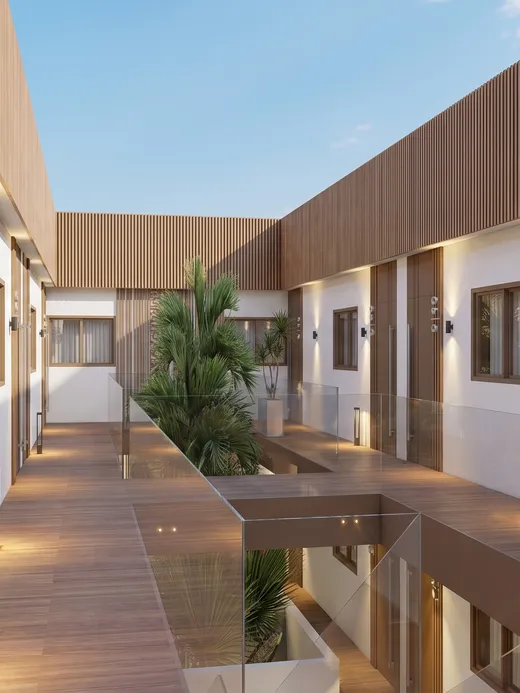 Sunlit view along the Thalassa Living courtyard walkway, with timber decking, glass railings, and palms growing at its center.