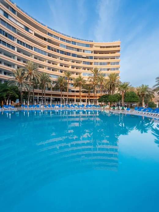 The curved seafront Marazul apartment building above its large blue pool lined with loungers.