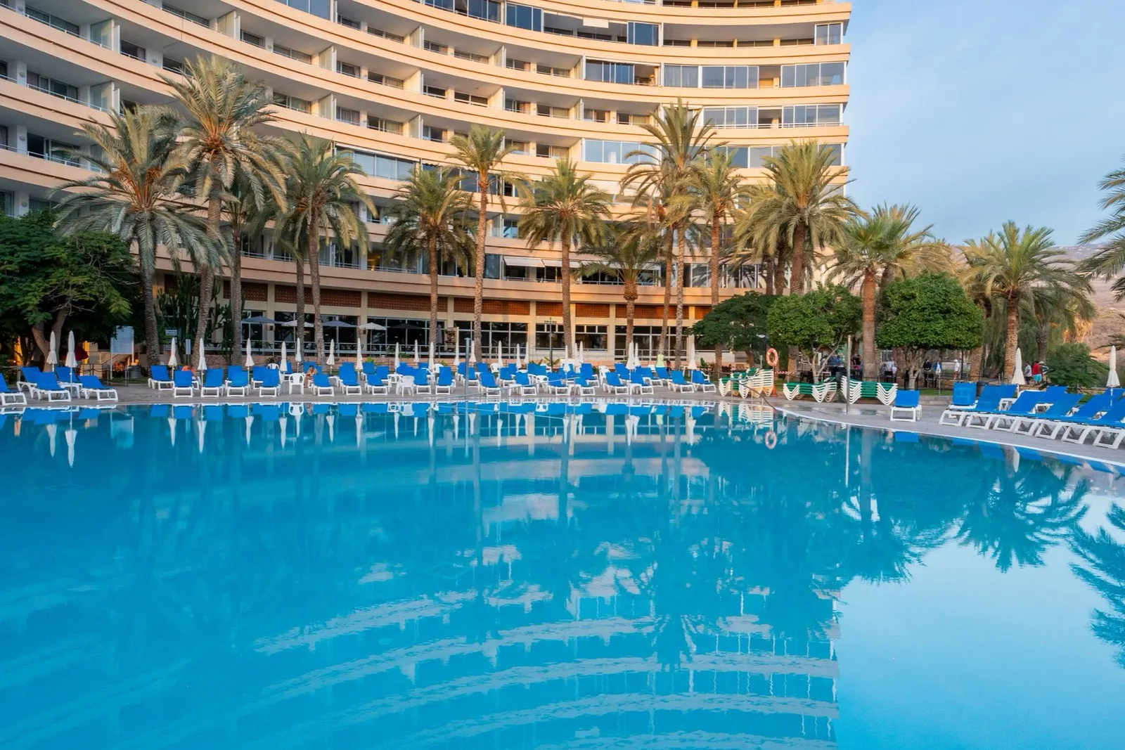 El edificio curvo de apartamentos Marazul frente al mar sobre su gran piscina azul con tumbonas.