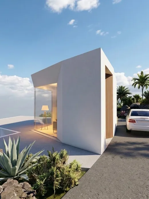 Driveway approach to the villa's angular white volume, framed by palms, agave, and volcanic rock outcrops with the ocean visible beyond.