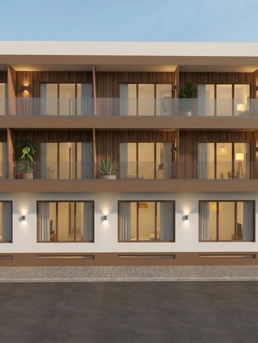 Front elevation of the Thalassa Living apartment building at dusk, with timber-lined balconies, potted plants, and the ground-floor entrance lit from within.