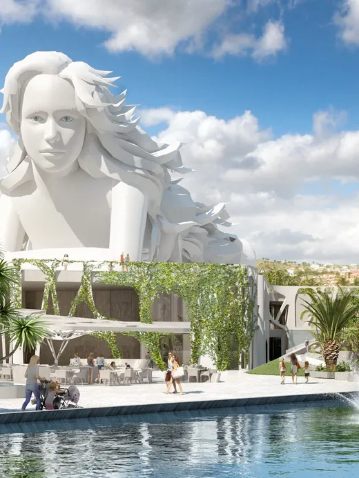 A monumental white sculpture of a woman's head and shoulders rising above a garden plaza with palms and fountains.