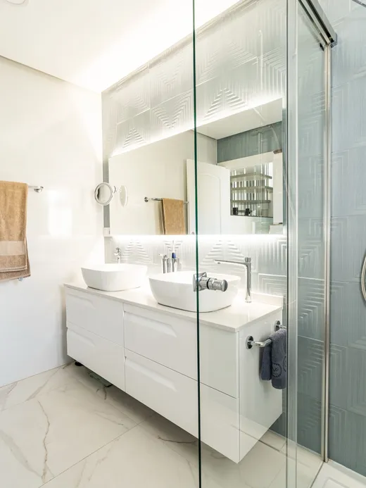 Bathroom with a double white vanity, a glass shower and textured teal wall tiles beside marble.