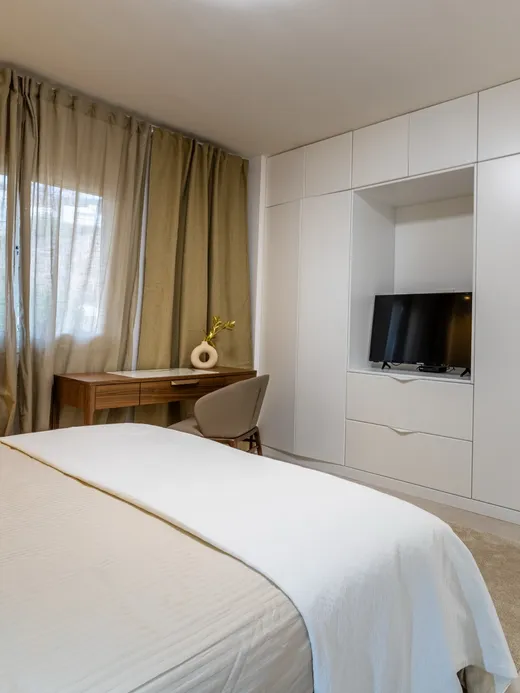 Bedroom in light beige with an oak-and-white fitted wardrobe, a desk and a TV niche.