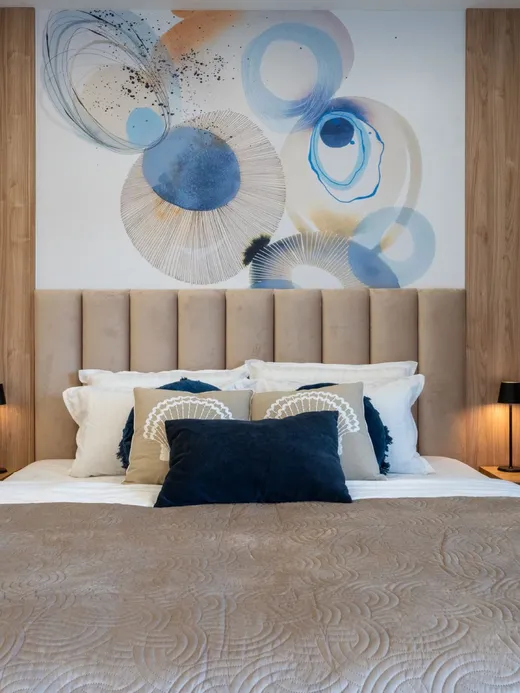 Bedroom with a timber headboard wall and a blue-and-gold circular abstract mural, flanked by black lamps.