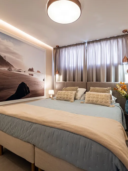 Bedroom with a black-sand beach photo mural above the bed, copper pendant lights and warm neutral bedding.