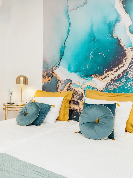 Bedroom with an emerald velvet bed and an oversized red-and-green fluid-art mural filling the headboard wall, with brass side tables.
