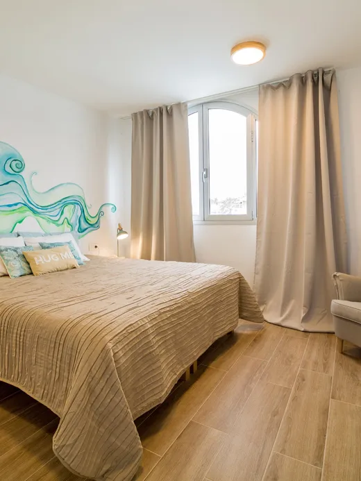 Bedroom with a flowing teal wave mural above the bed, brass reading lamps and an upholstered armchair.