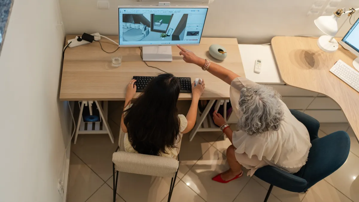 Two colleagues, seen from above, reviewing a photorealistic 3D interior render together on a computer screen.