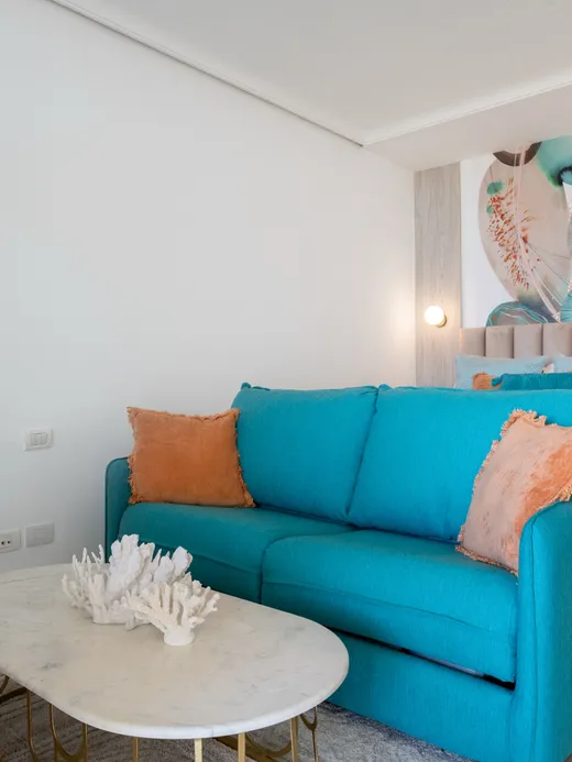 Dining nook with tan velvet chairs and a fluid coral-and-green mural, beside a sea-view window.