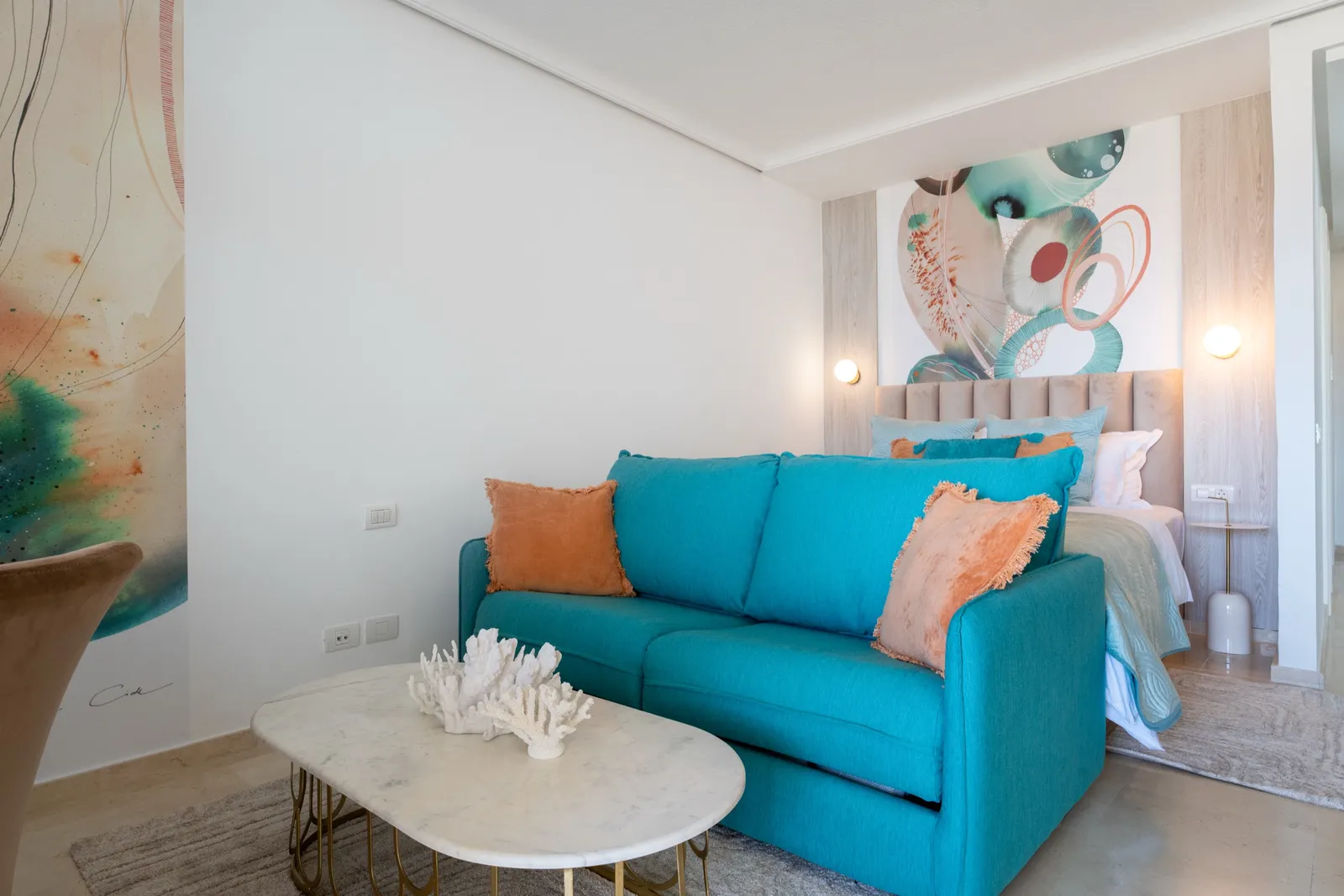 Dining nook with tan velvet chairs and a fluid coral-and-green mural, beside a sea-view window.