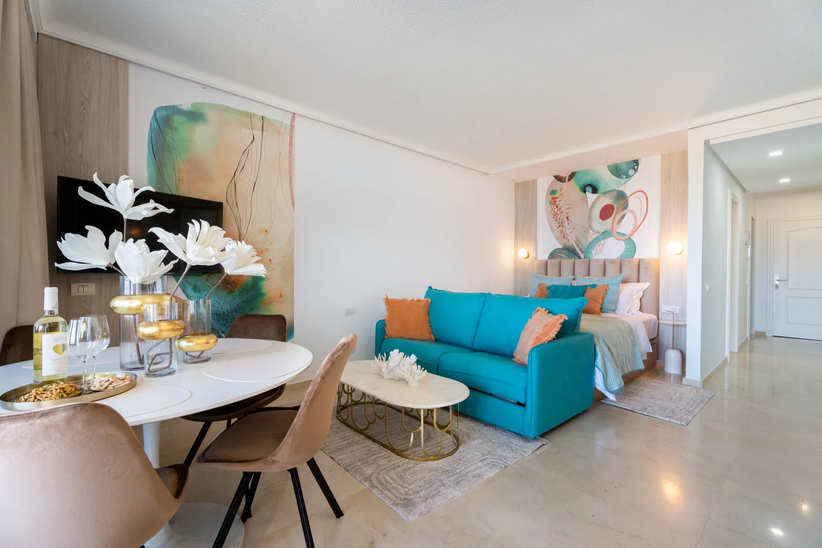 Living and dining space in coral and turquoise, with a teal sofa, coral-toned abstract murals, white coral-branch decor and marble floors.