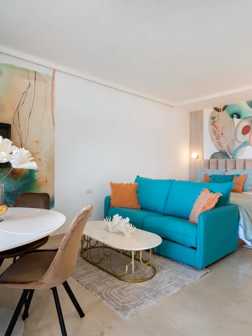 Living and dining space in coral and turquoise, with a teal sofa, coral-toned abstract murals, white coral-branch decor and marble floors.