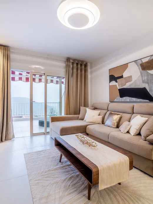 Living room in light beige and oak with a soft sofa, muted brown-and-black abstract art and a sea-view balcony.