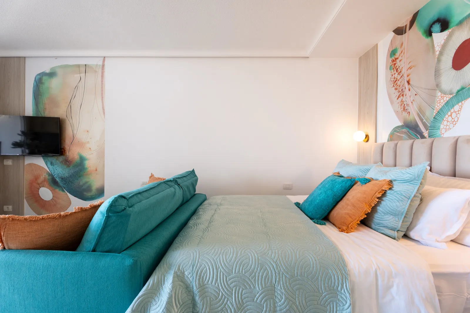 Living area with a teal sofa against a coral-and-blue art wall, a marble coffee table and white coral decor.
