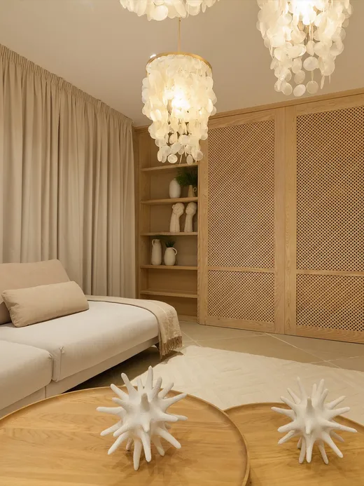 Neutral living room with a cream sofa, cane-screened wardrobe joinery and a capiz-shell chandelier.