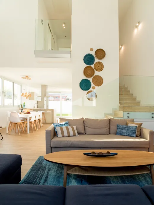 Open-plan living and dining space lit by round ceiling skylights, with a navy sofa, an oval timber coffee table and a floating stair.