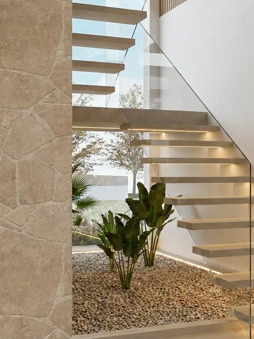 Floating stone staircase rising beside a glass balustrade, with a sunken pebble planter and a split-face stone column at its base.