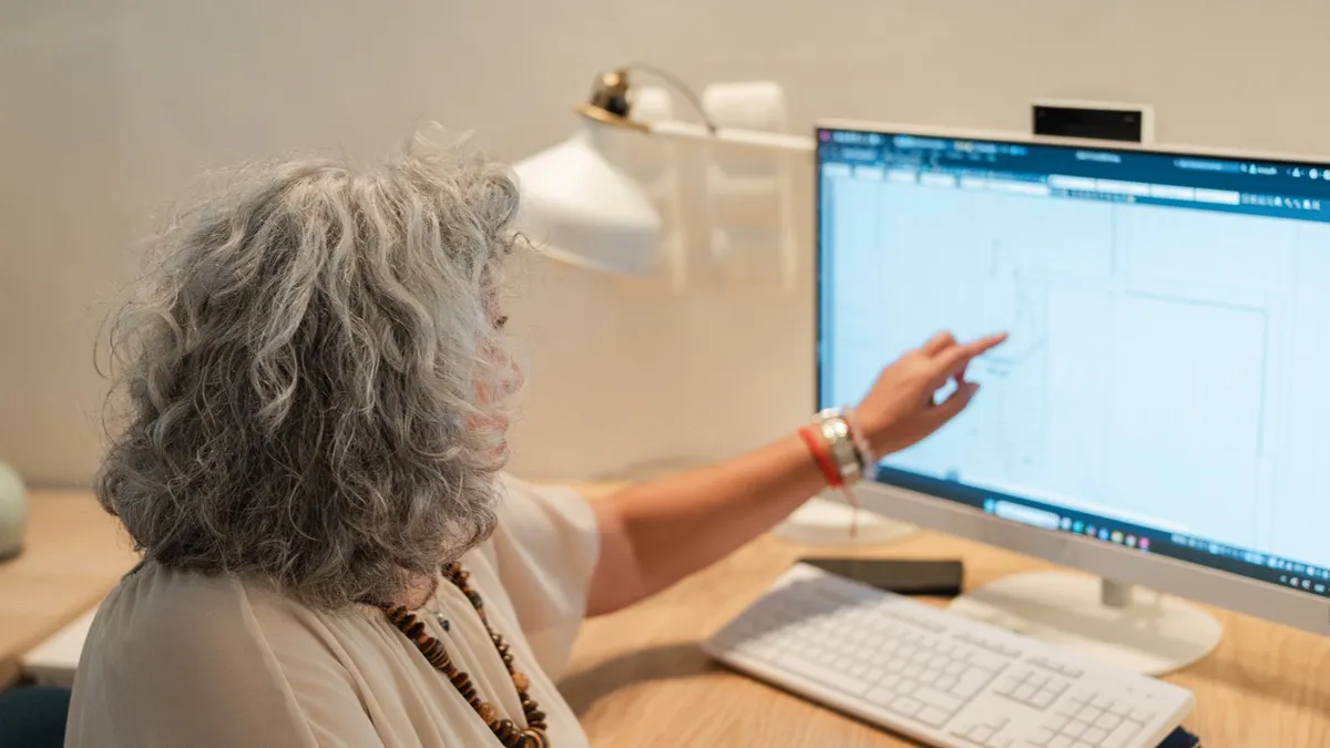 Rosa, seen from behind, pointing to a technical drawing open on her computer screen.