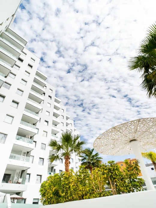 Large curved pool with a decorative blue-green mosaic water wall, surrounded by palms and the apartment blocks.