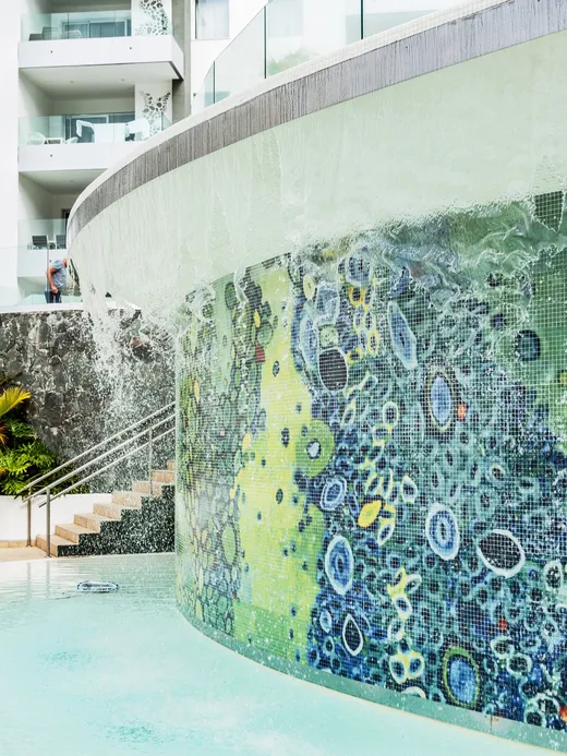 Close view of the mosaic water wall spilling into the pool beside a planted rockery.